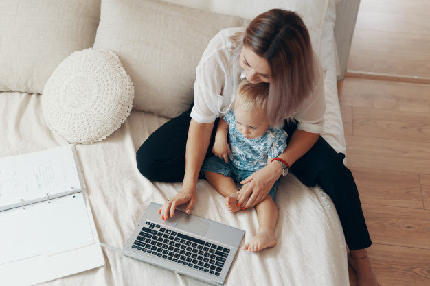 A Women with her baby working on laptop sitting over a bed